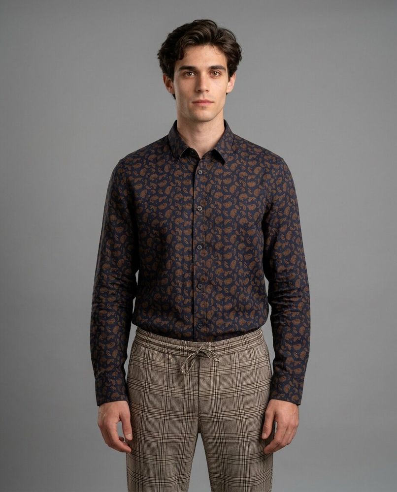 A male model in a grey studio wearing the same paisley shirt and check trousers