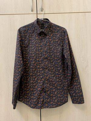 A brown paisley shirt photographed on a wire hanger against a wardrobe door