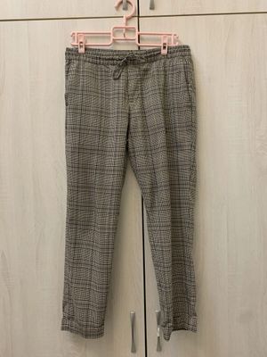 Grey check drawstring trousers photographed on a pink hanger against a wardrobe door