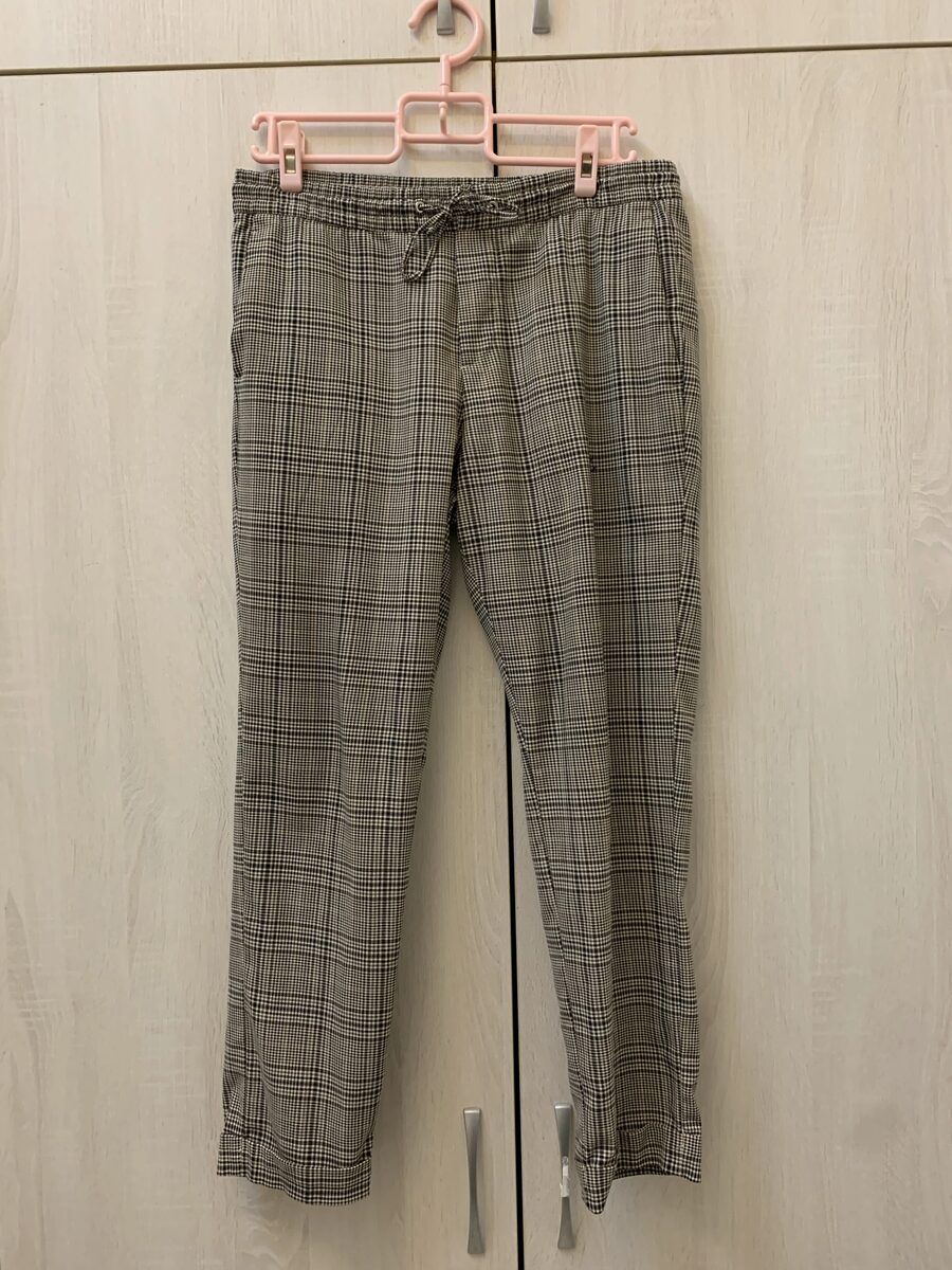 Grey check drawstring trousers photographed on a pink hanger against a wardrobe door